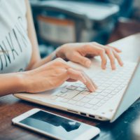 beautiful young hipster woman's hands busy working on her laptop sitting at wooden table in a coffee shop