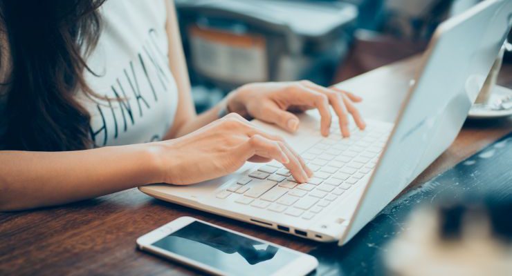 beautiful young hipster woman's hands busy working on her laptop sitting at wooden table in a coffee shop